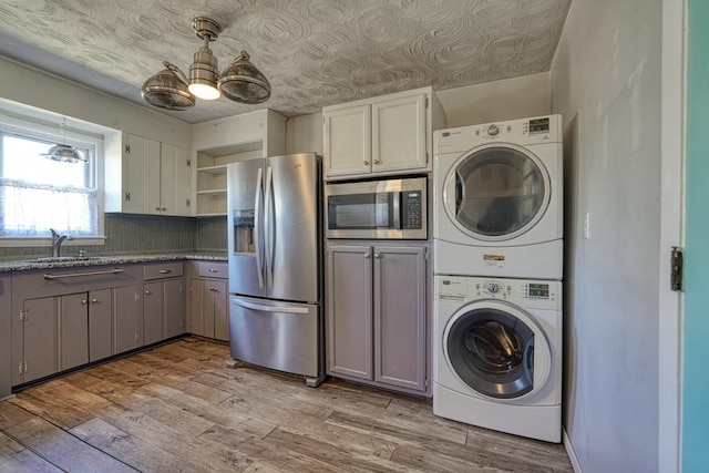 laundry area featuring stacked washer / drying machine, laundry area, a sink, and light wood finished floors