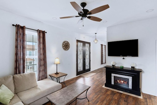 living area with french doors, a lit fireplace, baseboards, and wood finished floors