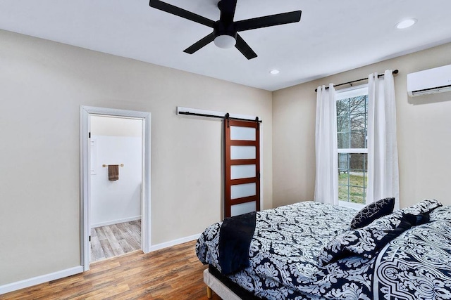 bedroom featuring a barn door, a wall mounted air conditioner, wood finished floors, and baseboards