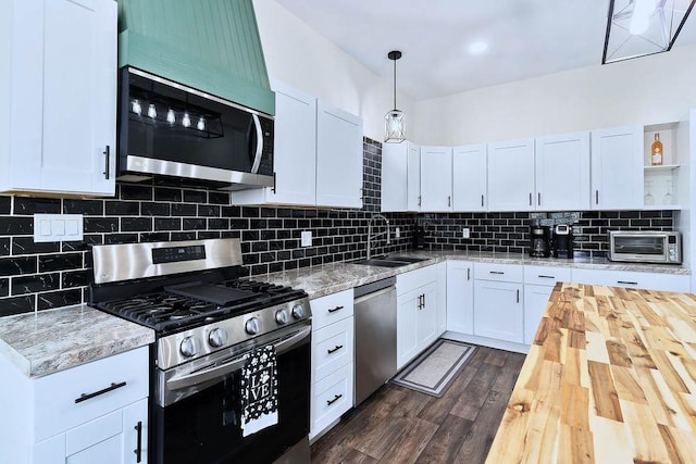 kitchen featuring dark wood finished floors, stainless steel appliances, decorative backsplash, a sink, and wood counters