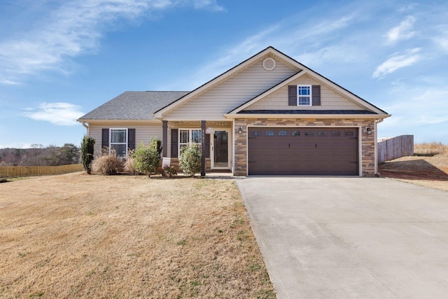 view of front of property featuring driveway, stone siding, fence, and a front yard