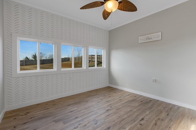 empty room with a healthy amount of sunlight, baseboards, crown molding, and wood finished floors