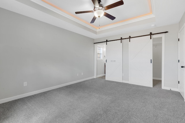 unfurnished bedroom with a raised ceiling, baseboards, and a barn door