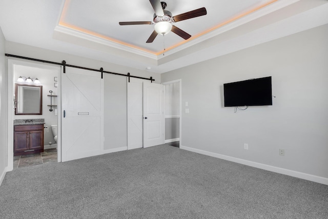 unfurnished bedroom with a raised ceiling, ensuite bathroom, a barn door, light carpet, and baseboards