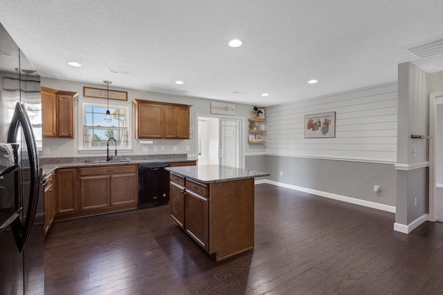 kitchen with dark stone counters, dark wood-style floors, a center island, black appliances, and a sink