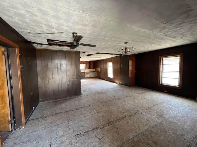 unfurnished room with an inviting chandelier, a wealth of natural light, and wooden walls