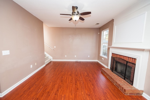 unfurnished living room featuring stairs, a ceiling fan, a fireplace, wood finished floors, and baseboards