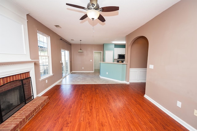 unfurnished living room featuring a ceiling fan, a fireplace, wood finished floors, baseboards, and visible vents