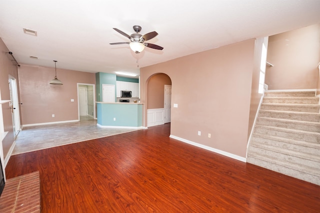 unfurnished living room with visible vents, baseboards, ceiling fan, wood finished floors, and arched walkways