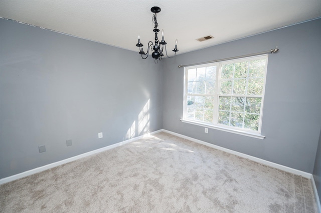 carpeted spare room featuring baseboards, visible vents, and a chandelier