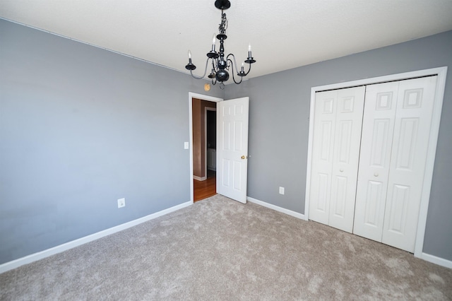 unfurnished bedroom featuring carpet flooring, a closet, a notable chandelier, and baseboards