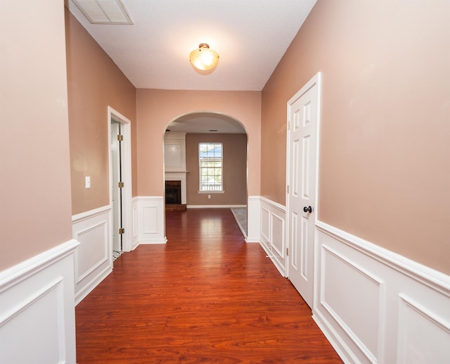 hall featuring visible vents, arched walkways, wainscoting, wood finished floors, and a decorative wall