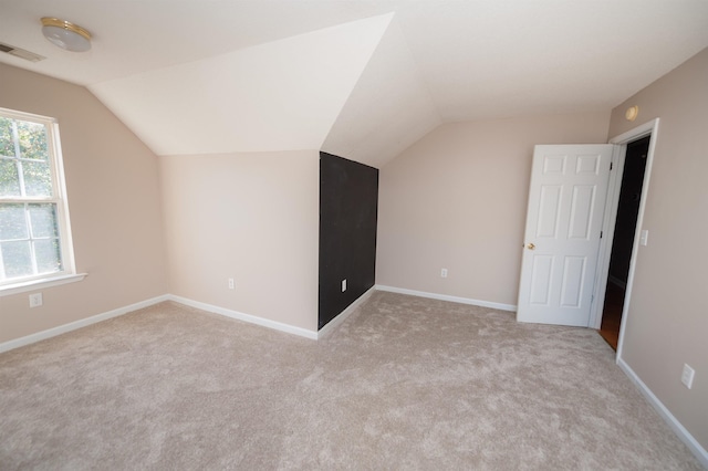 additional living space with baseboards, lofted ceiling, visible vents, and light carpet