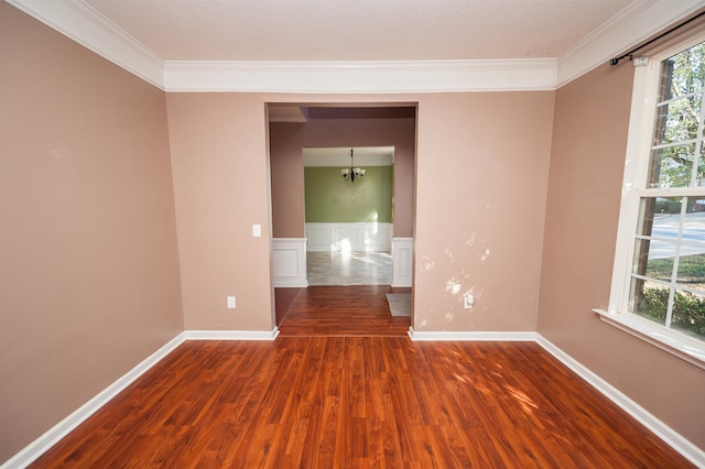unfurnished room with baseboards, wood finished floors, ornamental molding, and a chandelier