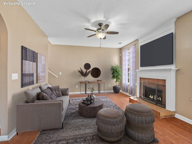 living room featuring a ceiling fan, arched walkways, a fireplace, and wood finished floors