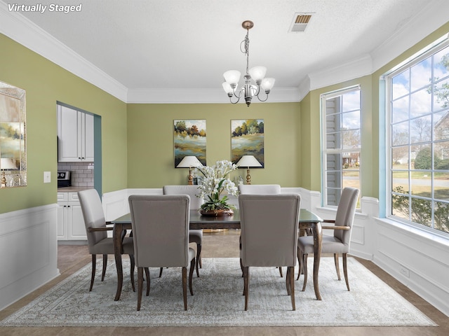dining space with a wainscoted wall, visible vents, crown molding, and a chandelier