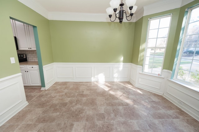 unfurnished dining area featuring a notable chandelier, a decorative wall, ornamental molding, and wainscoting