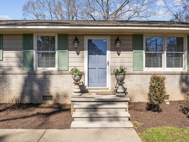 view of exterior entry featuring crawl space and brick siding