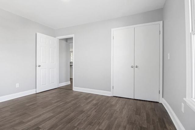 unfurnished bedroom featuring a closet, dark wood-style flooring, and baseboards