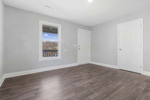 spare room with dark wood-style floors, visible vents, and baseboards