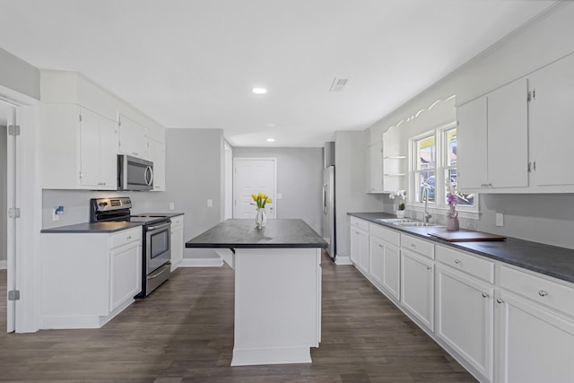 kitchen with dark countertops, a center island, stainless steel appliances, white cabinetry, and a sink