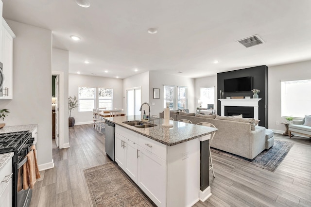 kitchen with a kitchen island with sink, a sink, visible vents, dishwasher, and black gas range oven