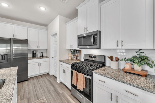 kitchen featuring stainless steel appliances, light wood-type flooring, white cabinetry, and tasteful backsplash