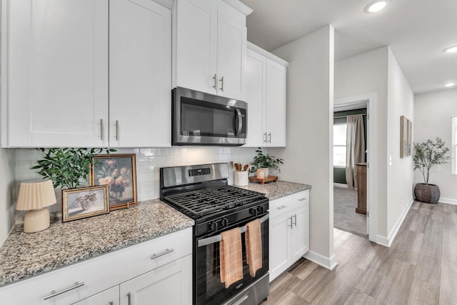 kitchen with stainless steel appliances, backsplash, white cabinetry, and light stone countertops