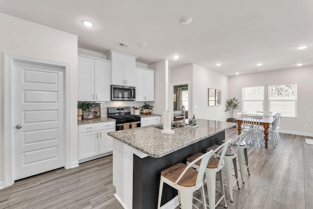 kitchen with appliances with stainless steel finishes, a breakfast bar, a kitchen island with sink, white cabinetry, and a sink