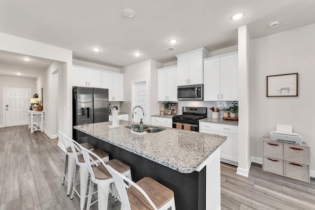 kitchen with appliances with stainless steel finishes, a sink, white cabinets, and a kitchen breakfast bar