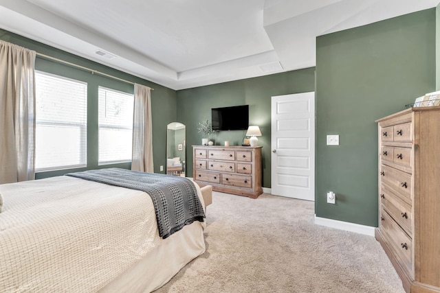 bedroom featuring visible vents, baseboards, arched walkways, a raised ceiling, and carpet flooring