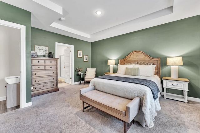 carpeted bedroom featuring a raised ceiling, connected bathroom, and baseboards