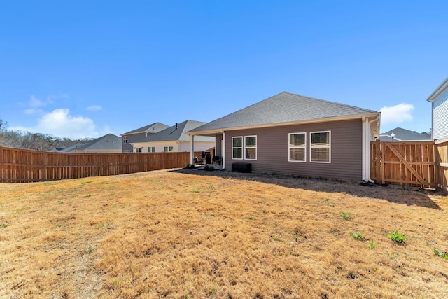 back of property with a fenced backyard, a shingled roof, central AC, and a yard