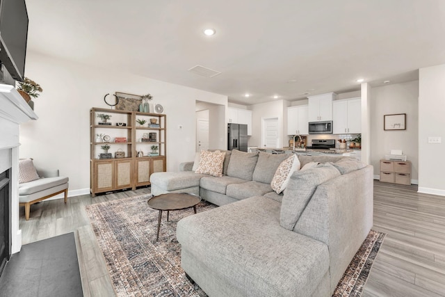 living room with light wood-type flooring, a fireplace, baseboards, and recessed lighting