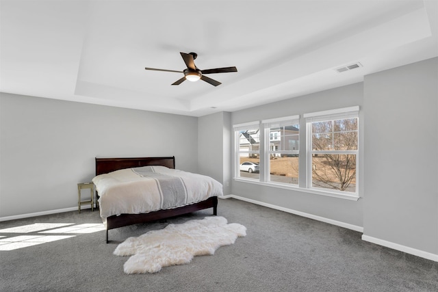 bedroom featuring a raised ceiling, visible vents, dark carpet, a ceiling fan, and baseboards