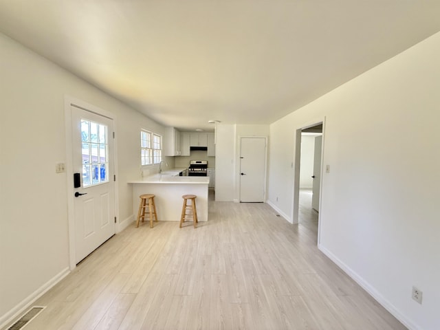 kitchen featuring visible vents, a breakfast bar, a peninsula, light countertops, and light wood-style floors