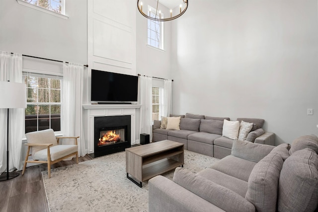 living area with a fireplace with flush hearth, wood finished floors, a wealth of natural light, and a chandelier