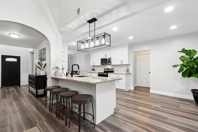 kitchen featuring visible vents, arched walkways, appliances with stainless steel finishes, a kitchen bar, and a sink