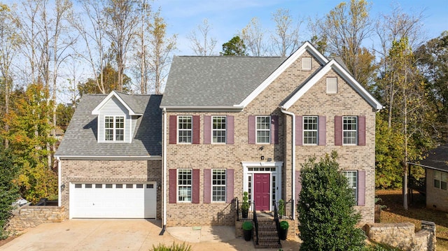 colonial inspired home with an attached garage, a shingled roof, concrete driveway, and brick siding