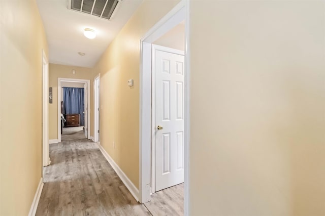 hall featuring light wood-style flooring, visible vents, and baseboards