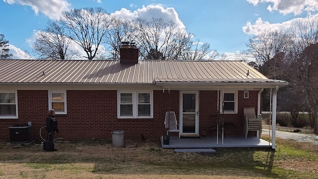 view of front of house featuring metal roof, central AC unit, brick siding, a front lawn, and a chimney