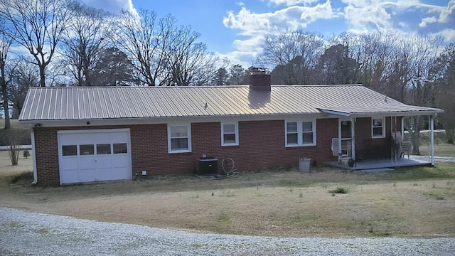 back of property featuring brick siding, a chimney, metal roof, a garage, and cooling unit