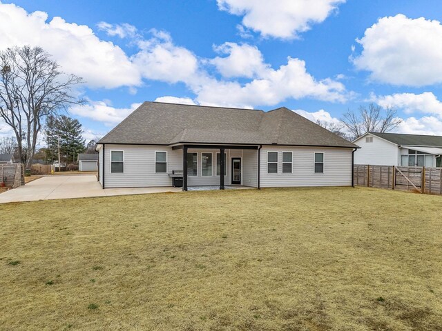 rear view of property featuring roof with shingles, a patio, fence, and a lawn