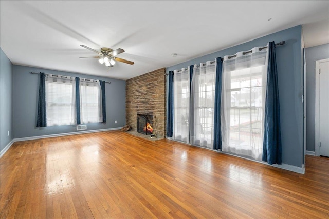 unfurnished living room featuring wood-type flooring, visible vents, a large fireplace, ceiling fan, and baseboards