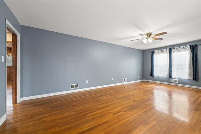 spare room with wood-type flooring, visible vents, ceiling fan, and baseboards