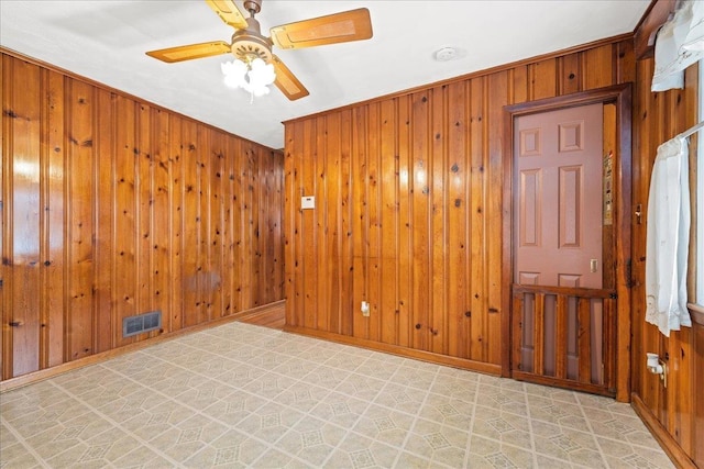 unfurnished room with ceiling fan, wooden walls, visible vents, baseboards, and tile patterned floors