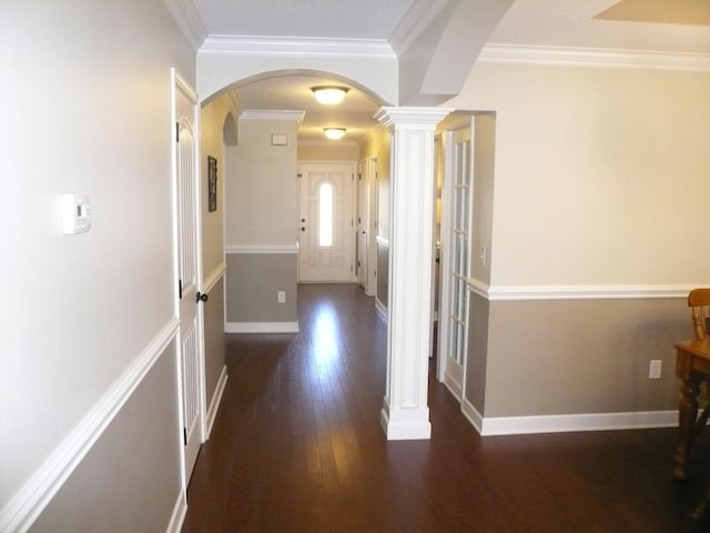 hallway with arched walkways, ornate columns, hardwood / wood-style floors, ornamental molding, and baseboards