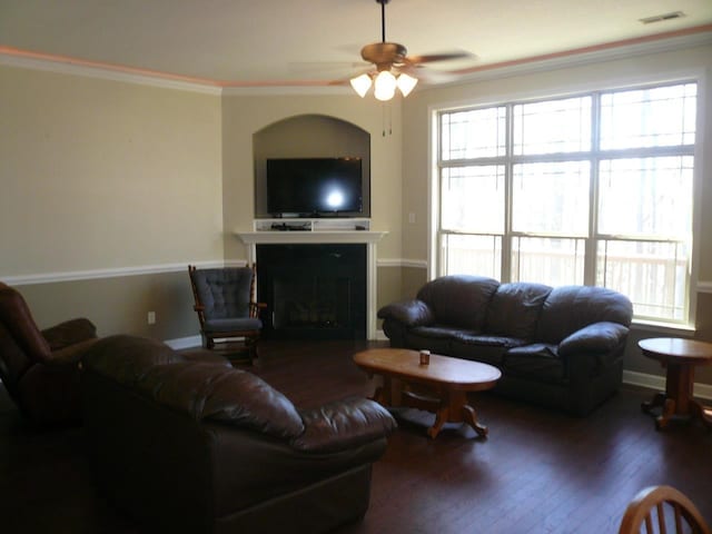 living room featuring a fireplace, wood finished floors, visible vents, a ceiling fan, and ornamental molding