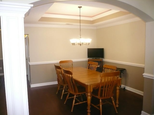 dining space with arched walkways, ornamental molding, wood finished floors, and a raised ceiling