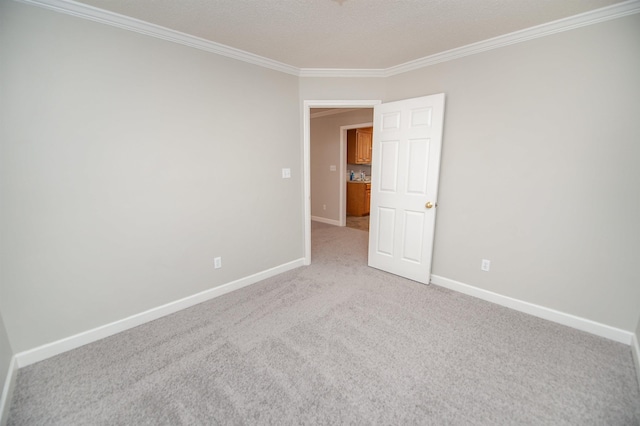 spare room featuring baseboards, ornamental molding, a textured ceiling, and light colored carpet